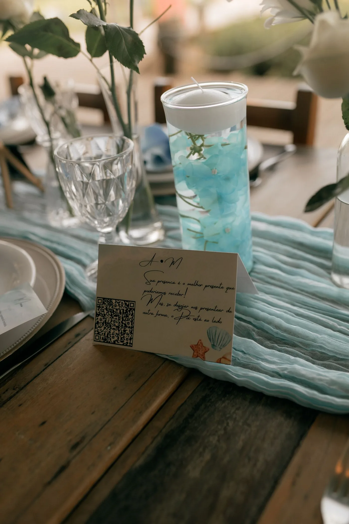 Eine Karte mit QR-Code steht auf einem gedeckten Hochzeitstisch zwischen Kerze und Blumen