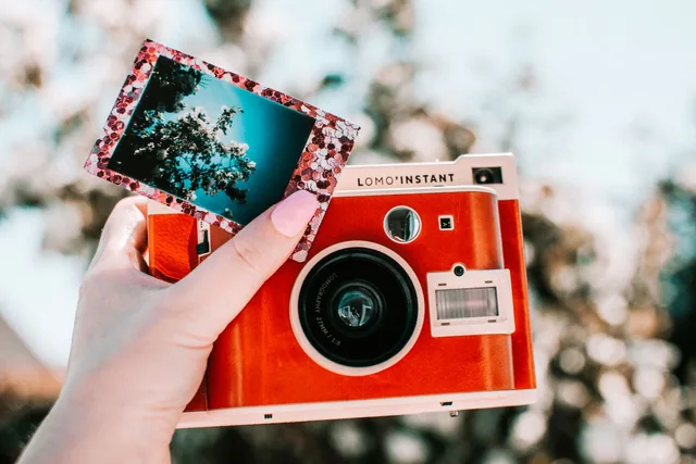 Hand hält eine rote Sofortbildkamera mit einem frisch entwickelten Foto